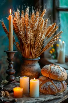 bread and candles on a table in front of a vase with wheat stalks, lit candles and other items