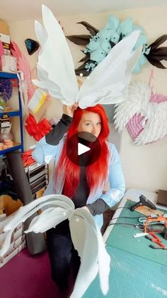 a woman with long red hair sitting in front of some paper birds on her head