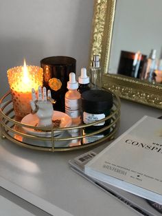 a candle and some bottles on a table next to a mirror with a magazine in front of it