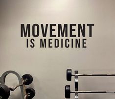 there is a gym wall with the words movement is medicine on it and dumbbells in front