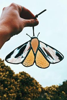 a hand holding a stained glass butterfly ornament with yellow and brown wings, against a blue sky