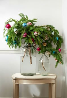 two glass vases with christmas ornaments on top of a table next to a wall