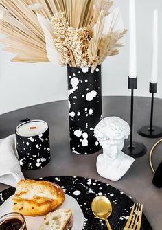 a black and white plate topped with bread next to a vase filled with wheat stalks