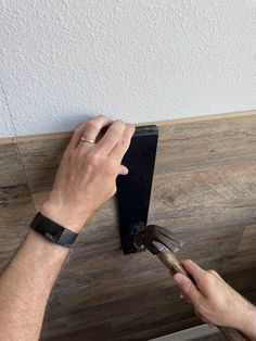 a man is working on a wood floor with a hammer and an adhesive tape