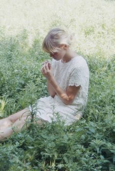 a woman sitting in the grass with her legs crossed and hands clasped to her chest