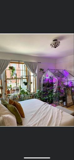 a bed with white sheets and pillows in a bedroom next to a window filled with potted plants