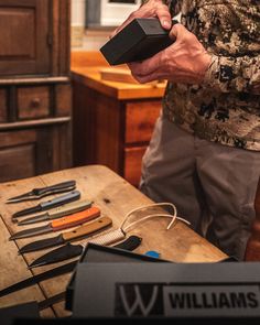 a man holding a black object on top of a wooden table next to other tools