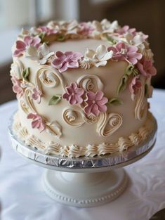 a white cake with pink and green flowers on it sitting on top of a table