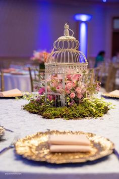 a birdcage filled with pink roses and greenery on top of a table