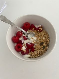 a bowl filled with granola, yogurt and raspberries next to a spoon