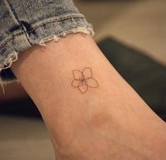 a small flower tattoo on the ankle is shown in black ink, and it looks like a four leaf clover