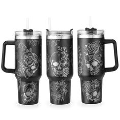 three black travel mugs with skulls and flowers on the front one has a straw in it