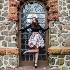 a woman standing in front of a window with her arms out and hands on her hips