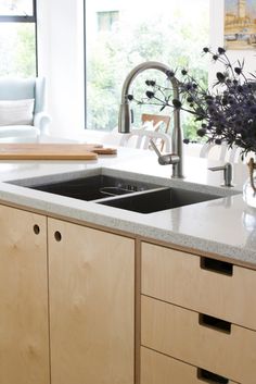 a kitchen sink sitting under a window next to a counter top with a vase filled with flowers