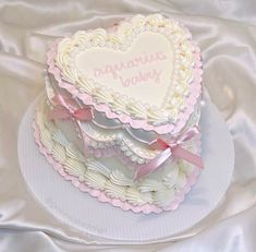 a heart shaped cake on top of a white platter with pink ribbon around the edges