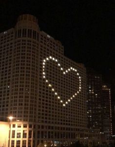 a large building with a heart drawn on it's side in front of the city at night