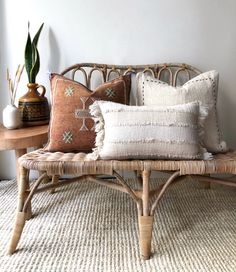 a wicker bench with pillows on it and a potted plant in the corner