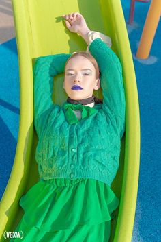 a doll in a green dress is laying on a yellow slide at a playground area