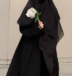 a woman in a nun outfit holding a white rose and wearing a black veil with her hands on her hips