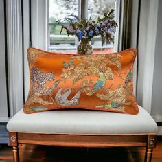 an orange pillow sitting on top of a white chair in front of a vase filled with flowers