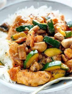 a white plate topped with chicken and veggies next to rice on top of a table