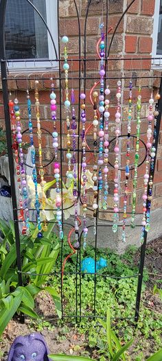 a purple stuffed animal sitting in the grass next to a metal pole with beads hanging from it