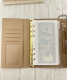 an open leather notebook with money inside on a white wooden table next to a pen and clipboard