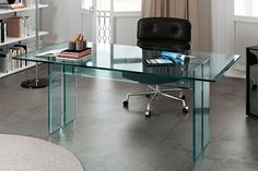 a glass desk with a black chair and bookshelf in the corner behind it