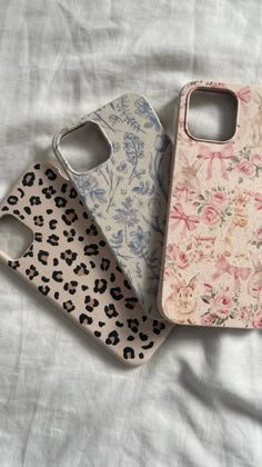 three cell phone cases sitting on top of a white bed covered in floral print fabric