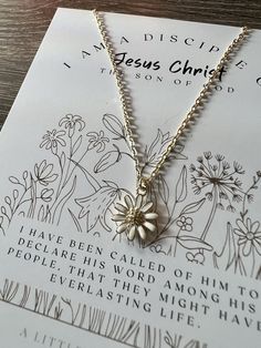 a necklace with a flower on it sitting on top of a piece of paper that says jesus christ