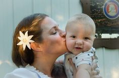 a woman kissing a baby with a flower in her hair