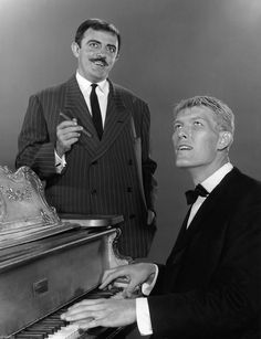 two men in suits are playing the piano and one is wearing a moustache