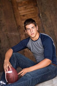 a young man sitting on the ground with a football in his hand and looking at the camera