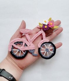 a hand is holding two miniature crocheted bicycles and a cupcake on it