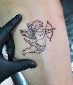 a small tattoo on the leg of a man with an angel holding a bow and arrow