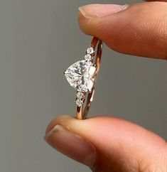 a woman's hand holding an engagement ring with a heart shaped diamond on it