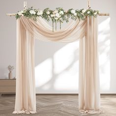 a wedding arch decorated with white flowers and greenery on the top, in front of a wall