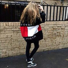 a woman standing in front of a brick wall wearing a tommy flag sweatshirt and black leggings