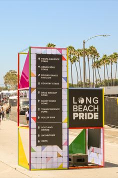 a sign that says long beach pride in front of palm trees and people walking on the sidewalk