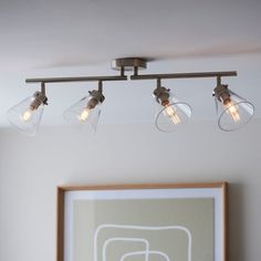 three lights are hanging from the ceiling above a framed art piece and a painting is on the wall