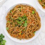 two bowls filled with noodles and carrots on top of a white table cloth next to silver utensils