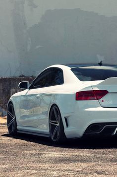 the rear end of a white car parked in front of a concrete wall with graffiti on it