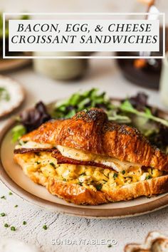 bacon, egg and cheese croissant sandwiches on a plate with salad in the background