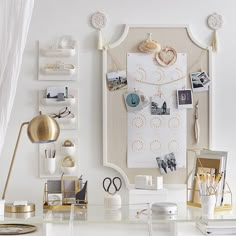 a white desk topped with lots of clutter next to a wall mounted art piece