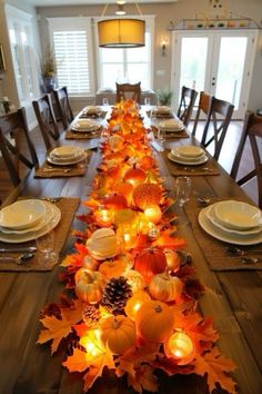 a long table is decorated with fall leaves and candles for the centerpiece in this dining room