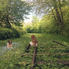 two young women sitting on the tracks next to each other in an overgrown forest area