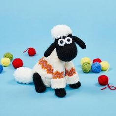 a knitted black and white sheep sitting in front of balls of yarn on a blue background