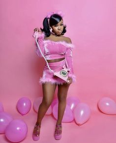 a woman in a pink outfit posing for a photo with balloons around her and holding a cell phone