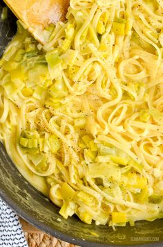 a pan filled with noodles and vegetables on top of a table next to a wooden spoon