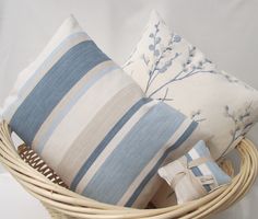 three decorative pillows in a basket on a white sheeted surface, one is blue and the other is beige